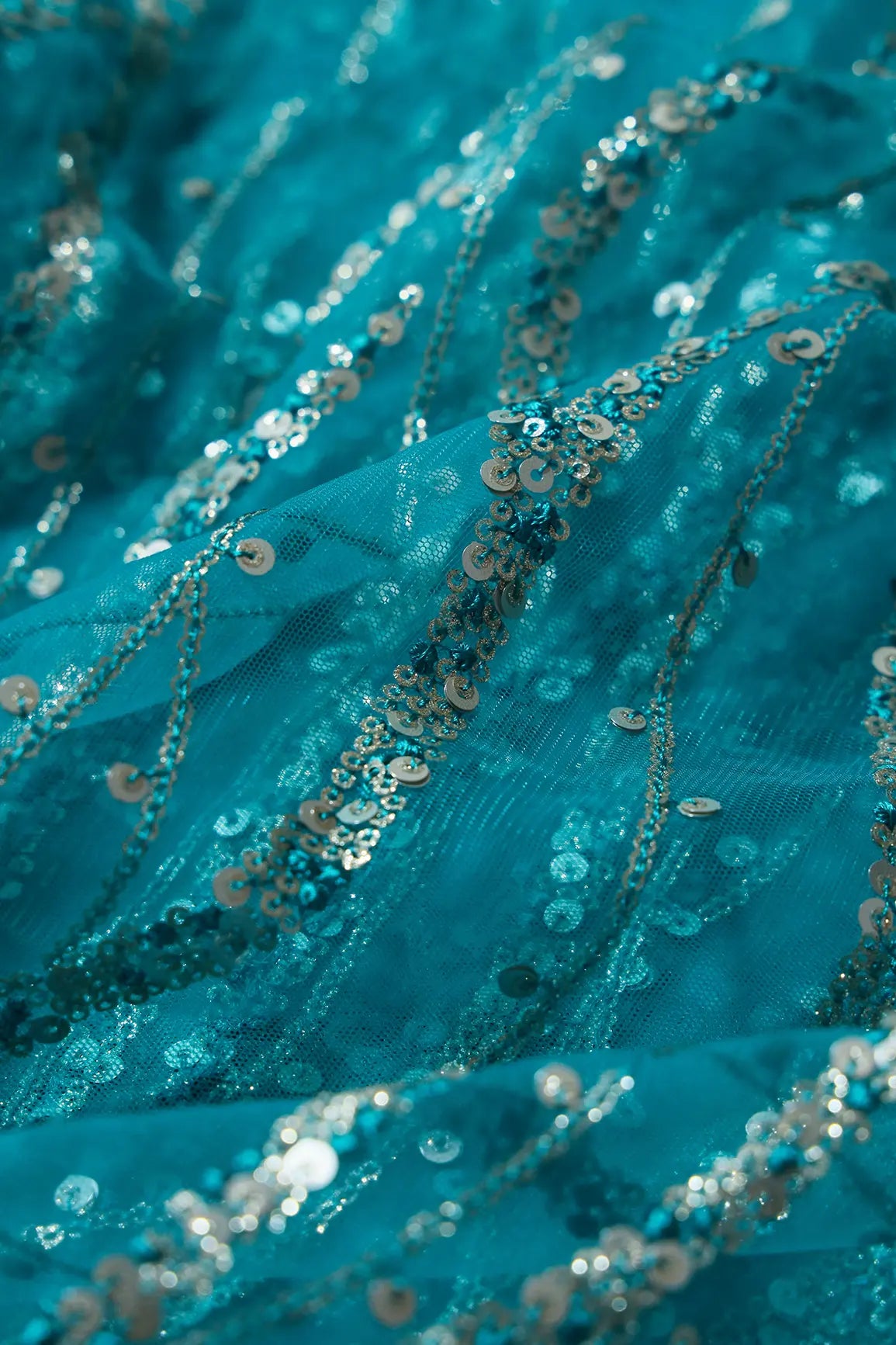 Gold And Silver Sequins With Peacock Blue Thread Wavy Embroidery On Peacock Blue Soft Net Fabric